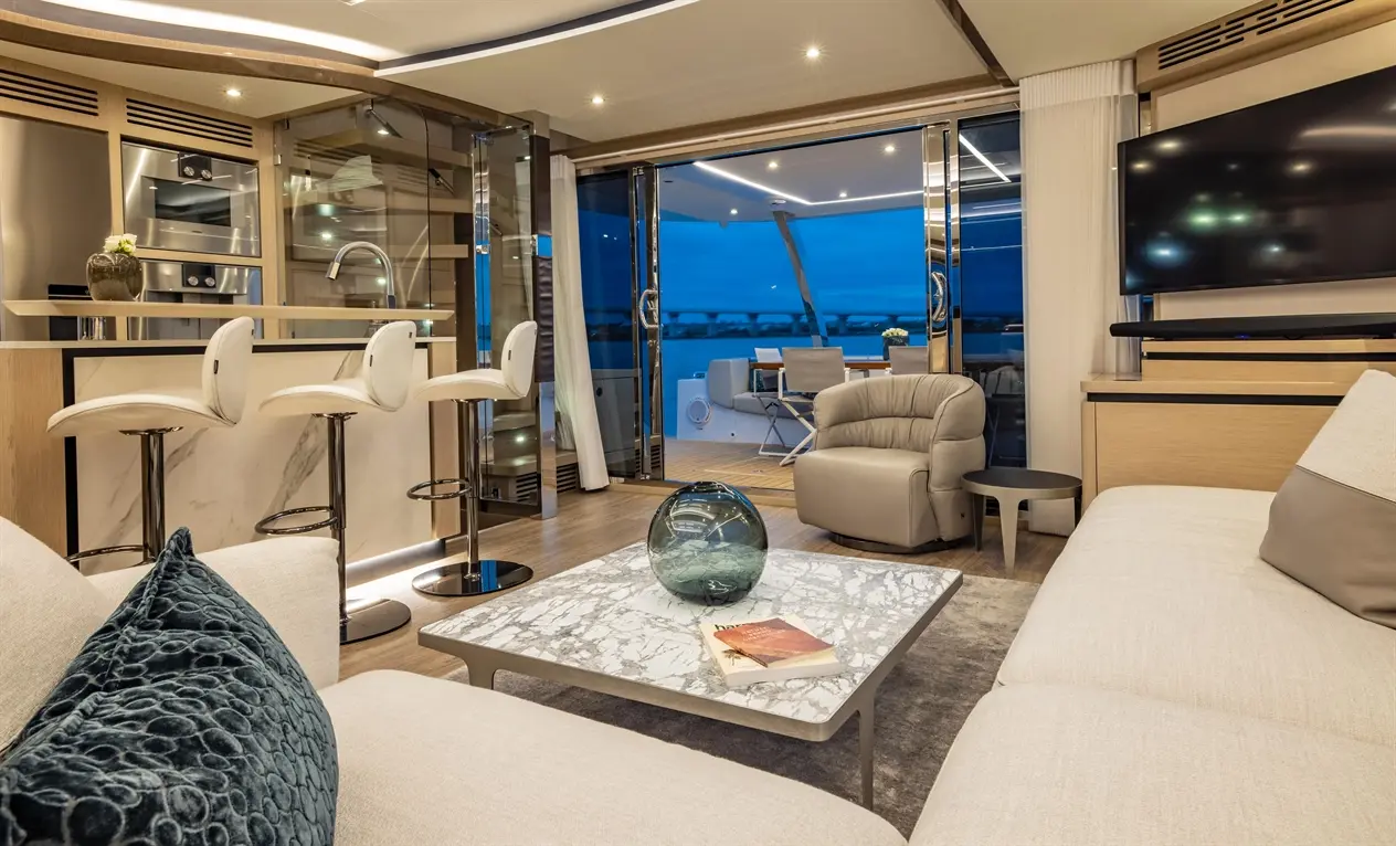 Modern living room with a marble table, bar stools, and large windows overlooking the water, showcasing stylish interior design.